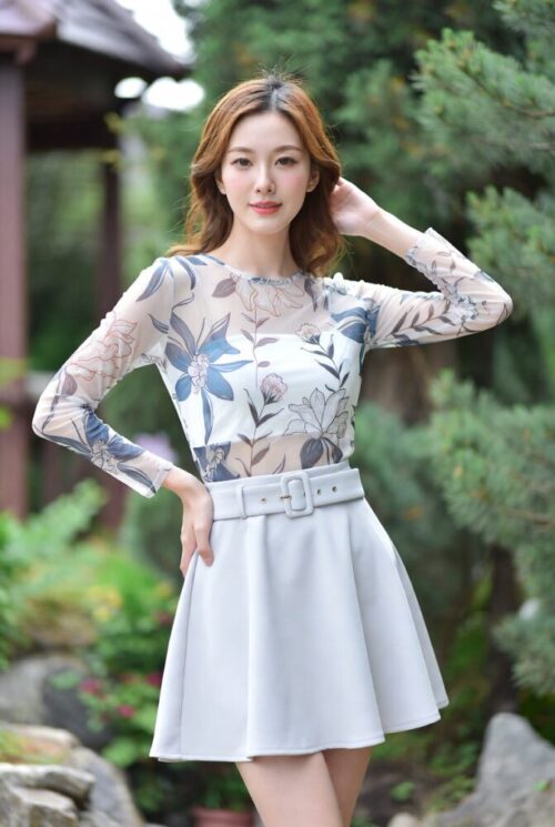 女性が自然の風景の中で、花柄のトップスとフレアスカートという夏の装いで屋外でポーズをとっている。