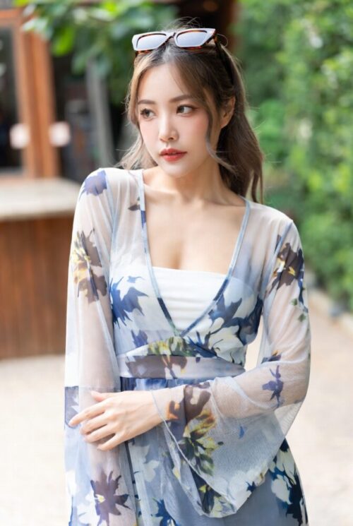 女性が夏服姿で屋外に立つ。透けるドレスを身にまとい、背景はカジュアルな風景である。