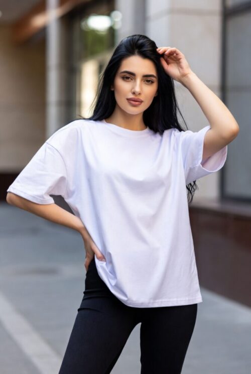 女性が都市の風景の中で、自然光の下でカジュアルな服装を着て、さりげなくポーズを取っている。